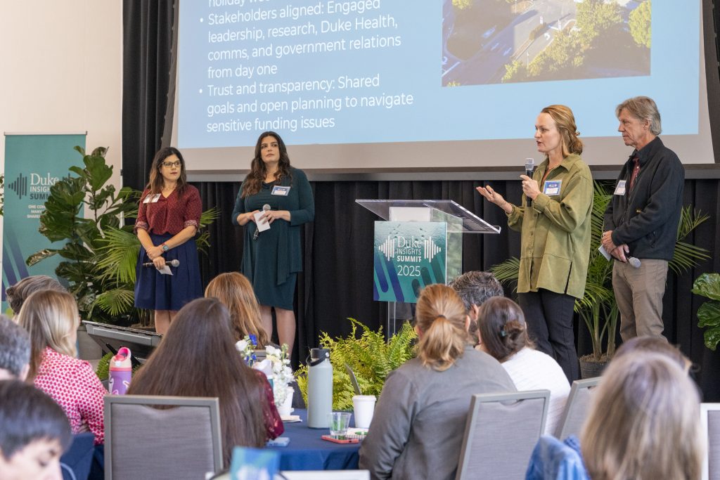 Julie Schoonmaker, Stephanie Lopez, Beth Berg and Dave Hart stand on stage in front of a slide about partnering on Duke Research Saves Lives