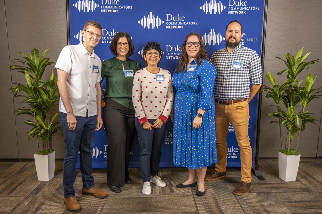 Five people from the Working@Duke team standing in front of the step and repeat